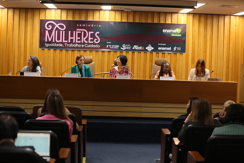 Foto do auditório com um publico diverso de mulheres na mesa.