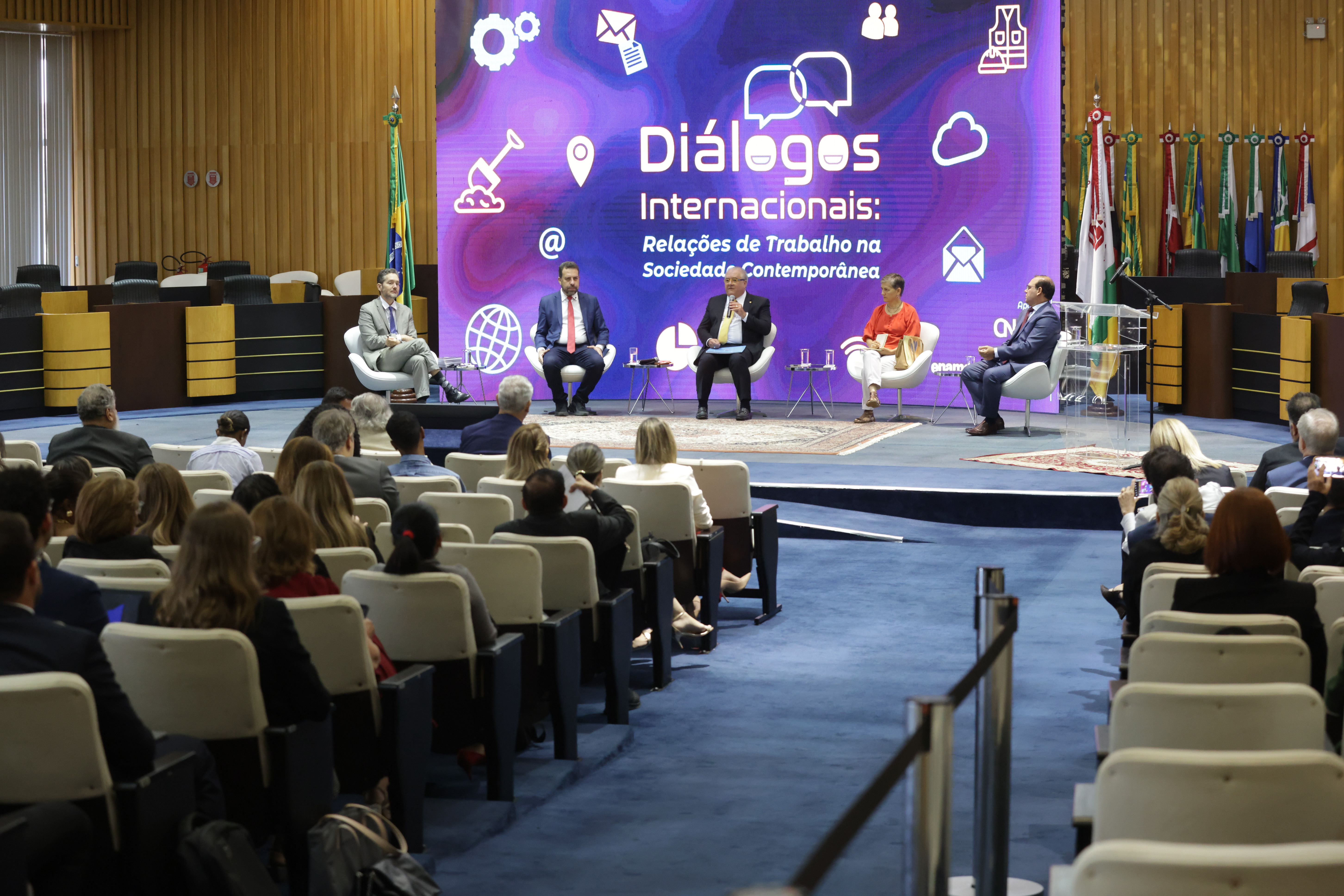 Participantes de painel do congresso sentados em cadeiras em semicírculo, diante da platéia