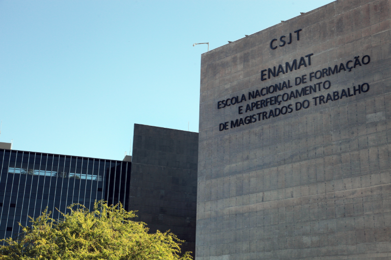 Foto da Fachada externa da Enamat. Um paredão de concreto com o nome da escola em letras caixas pretras.