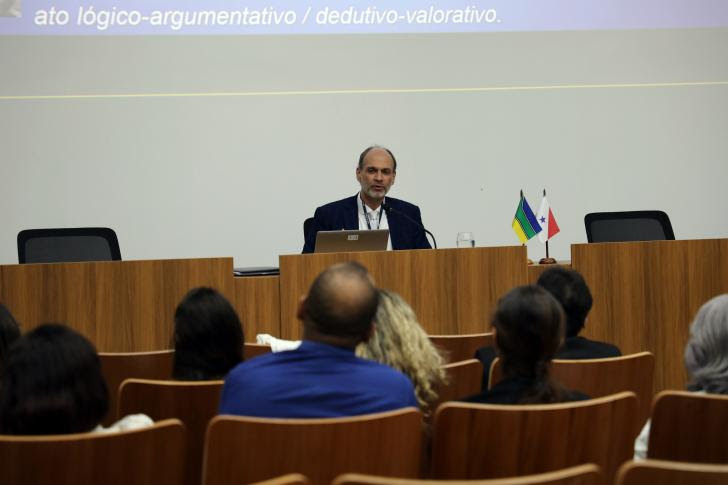 Foto de homem sentado na mesa do evento falando para a plateira